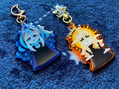 two key chains with cartoon characters on them sitting next to each other in front of a blue carpet