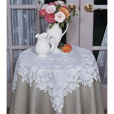 a white vase with flowers in it sitting on a table next to a window and curtain