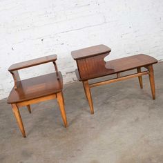 two wooden chairs sitting next to each other in front of a white brick wall and cement floor