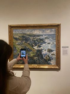 a woman taking a photo of a painting with her phone