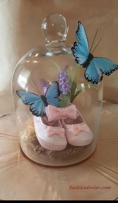 two blue butterflies sitting on top of pink baby shoes under a glass clochet