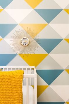 a white crib with a yellow blanket on top of it in front of a colorful wall