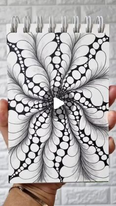 someone holding up a spiral notebook with black and white designs