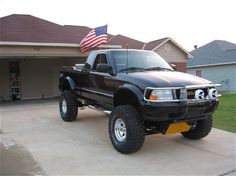 a black pickup truck parked in front of a house with an american flag on the roof