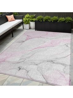 a pink and gray area rug on top of a patio with potted plants in the background