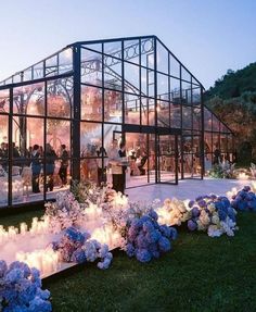 a group of people standing in front of a glass building with flowers and candles on the ground