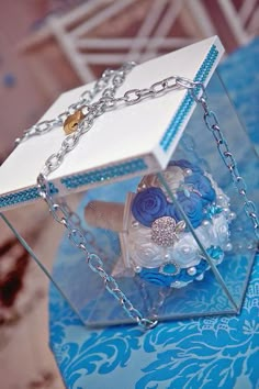 a blue and white wedding bouquet in a glass box on a table with a chain around it