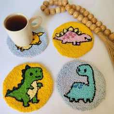 three coasters with dinosaurs on them next to a coffee cup and bead necklace