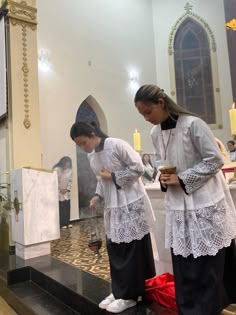 two women standing in front of a shrine with candles on the altar and one holding a cup