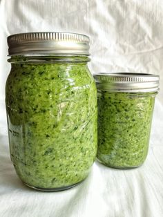 two jars filled with green sauce sitting on top of a white cloth