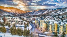 the town is surrounded by mountains and snow covered trees in the foreground, with buildings on either side