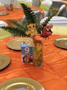 a table with plates, silverware and an orange table cloth has a lion centerpiece on it