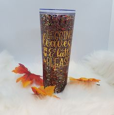 a glitter tumbler sitting on top of a white fur covered floor next to autumn leaves