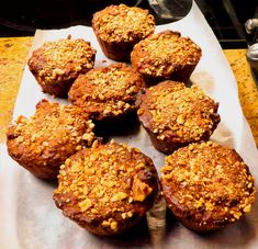 some muffins are sitting on top of a piece of parchment paper with crumbled toppings