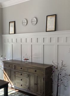 a wooden dresser sitting in the corner of a living room next to a wall with pictures on it