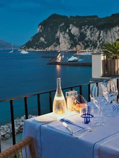 the table is set with wine and glasses on it, overlooking the water's edge