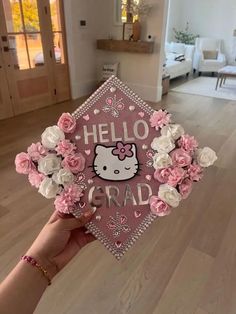 someone is holding up a pink graduation cap with hello kitty on it and flowers in the middle