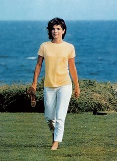 a young man walking across a lush green field next to the ocean on a sunny day