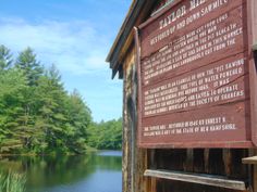 a sign on the side of a wooden building next to a body of water with trees in the background