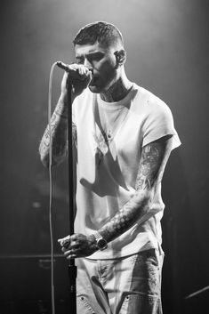 a man with tattoos on his arm holding a microphone and standing in front of a stage