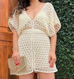 a woman standing in front of a wooden wall wearing a white crochet dress