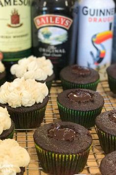 chocolate cupcakes with white frosting on a cooling rack next to bottles of booze