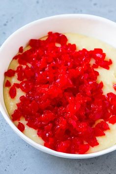 a white bowl filled with red toppings on top of a blue countertop next to a knife and fork