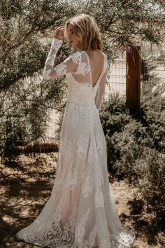 a woman in a wedding dress standing under a tree with her back to the camera