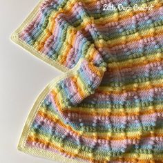 a crocheted sweater is laying on top of a white surface and it has multicolored stripes