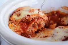 a white bowl filled with lasagna sauce and meat covered in grated cheese