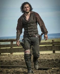 a man with long hair and no shirt is walking in the dirt near a fence