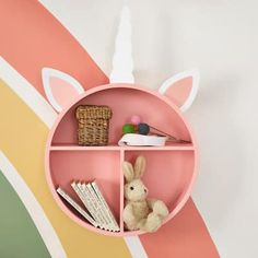 a pink shelf with some books and stuffed animals on it in front of a rainbow painted wall