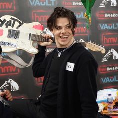 a young man holding an electric guitar in his right hand and smiling at the camera