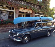 an old station wagon with a surfboard on the roof parked in front of a coffee shop