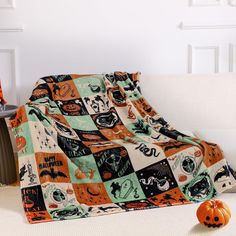 an orange and black blanket sitting on top of a white couch next to a pumpkin