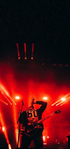 a man standing on stage with his guitar in front of red and white lights behind him