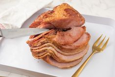 a white plate topped with sliced ham next to a knife and fork