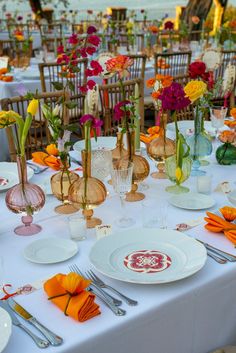 the table is set with plates, silverware and vases filled with colorful flowers