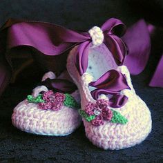 crocheted baby shoes with bows and flowers on them, sitting next to a purple ribbon