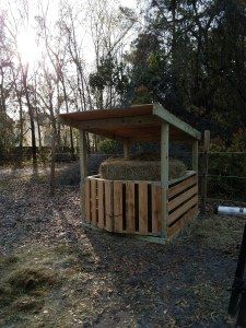 a small wooden structure in the middle of a field with trees and bushes behind it