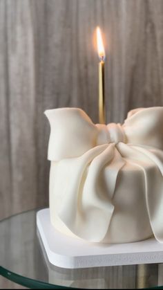 a white cake with a bow on top and a candle in the middle, sitting on a glass table