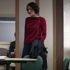 a woman standing in an office with her back to the camera, wearing a red sweater