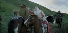 two people riding on horses in the middle of a field with other people walking behind them