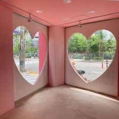 two heart - shaped windows in a pink room with the reflection of a street and trees