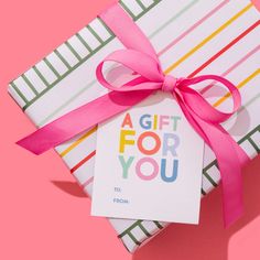 a gift for you is wrapped in colorful paper and tied with a pink ribbon on a pink background