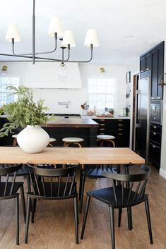 a dining room table with chairs and a vase on top of it in the middle of a kitchen