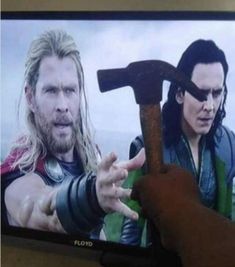 a man holding an ax in front of a tv screen with the image of thor and loki on it