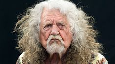 an old man with long white hair and beard wearing a floral shirt looking at the camera