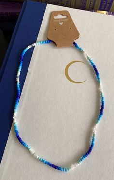 a blue and white beaded necklace sitting on top of a book with a tag