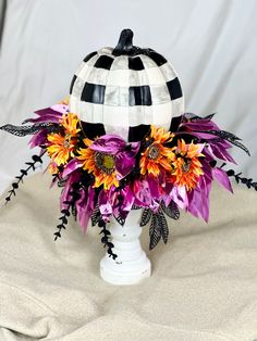 a white vase filled with purple and orange flowers on top of a tablecloth covered surface